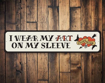 May include: White metal sign with black text that reads "I wear my art on my sleeve". The sign features a red heart with the words "Yours" and "Mine" on it.