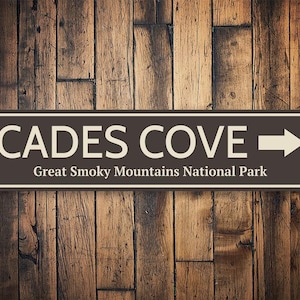 May include: Brown and white sign with the text "Cades Cove" and "Great Smoky Mountains National Park". An arrow points to the right.