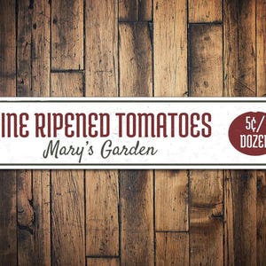 May include: White metal sign with red text that reads "Vine Ripened Tomatoes Mary's Garden 5¢/Dozen".