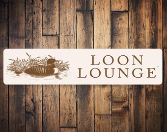 Puede incluir: Un letrero blanco con texto marrón y una ilustración marrón de un colimbo nadando en un lago. El letrero dice "LOON LOUNGE".