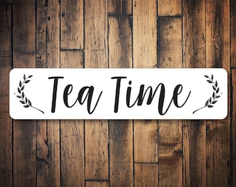 Könnte beinhalten: Ein weißes rechteckiges Schild mit schwarzem Text und Blattdesigns auf beiden Seiten, auf dem "Tea Time" steht.