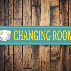 May include: A blue and yellow metal sign with the text "CHANGING ROOM" in yellow letters. A white nappy with yellow stars is on the left side of the sign.
