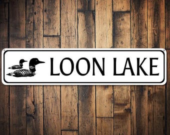 Puede incluir: Un letrero rectangular blanco con texto negro y una silueta negra de dos loons. El letrero dice "LOON LAKE".