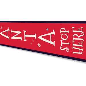 May include: Red metal sign with white text that reads "Santa Stop Here" with blue snowflake accents.