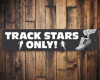 Puede incluir: Un letrero en blanco y negro con el texto "TRACK STARS ONLY!" en letras blancas. El letrero presenta un zapato para correr con alas y dos figuras de palo corriendo.
