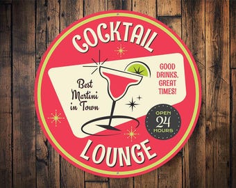 Op de afbeelding: Een rond bord in rood en geel met de tekst "Cocktail Lounge" in een retro-lettertype. Het bord toont een martini-glas met een limoenwig en de tekst "Best Martini in Town". Het bord bevat ook de tekst "Good Drinks. Great Times!" en "Open 24 Hours".