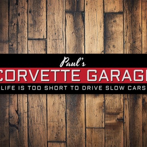 May include: Black and red metal sign with white text that reads "Paul's Corvette Garage - Life is too short to drive slow cars."