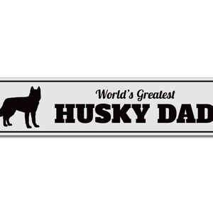 May include: A white metal sign with a black silhouette of a husky dog and the text "World's Greatest Husky Dad".