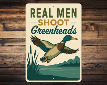 Może przedstawiać: Prostokątny metalowy znak z napisem "REAL MEN SHOOT Greenheads" nad ilustracją lecącej kaczki. Kaczka jest brązowa, beżowa i zielona, z żółtym dziobem. Tło przedstawia jezioro i drzewa.