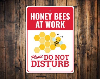 May include: A rectangular sign with a red top section that reads "HONEY BEES AT WORK" in white. Below is a white section with a yellow honeycomb and a cartoon bee. The bottom section reads "Please DO NOT DISTURB" in red.