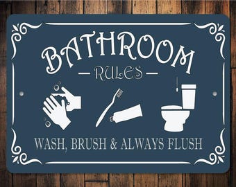 May include: Blue bathroom sign with white text and icons. The sign reads "Bathroom Rules - Wash, Brush & Always Flush". The icons depict hand washing, tooth brushing, and a toilet.