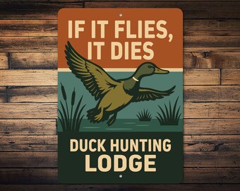 Może przedstawiać: Prostokątny metalowy znak z kaczką w locie nad wodą, z napisem "IF IT FLIES, IT DIES" u góry i "DUCK HUNTING LODGE" na dole. Znak ma rustykalny design z brązową, zieloną i pomarańczową kolorystyką.