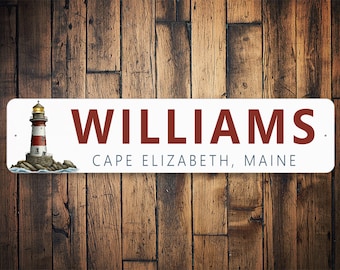 May include: White metal sign with red text that reads "WILLIAMS, CAPE ELIZABETH, MAINE". A lighthouse with a red and white striped tower is pictured on the left side of the sign.