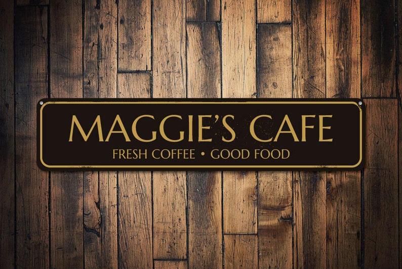 Pu&ograve; includere: Segno nero e dorato con il testo "Maggie's Cafe" e lo slogan "Fresh Coffee - Good Food".