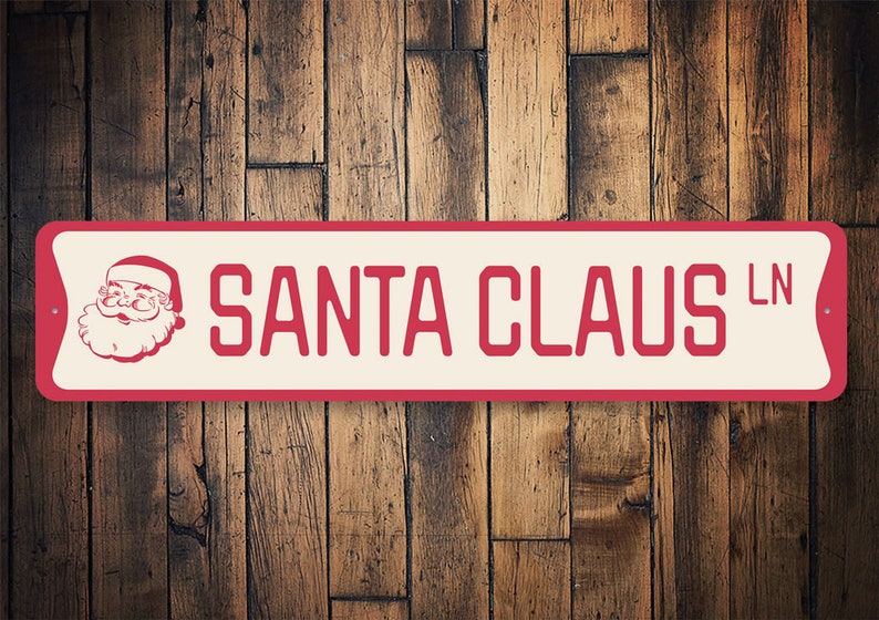 Op de afbeelding: Rood en wit metalen bord met een afbeelding van de kerstman en de tekst "SANTA CLAUS LN".