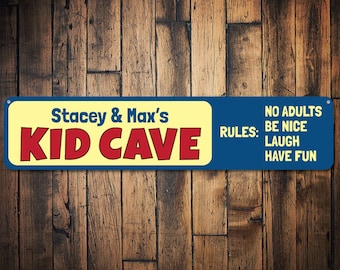 May include: A blue and yellow sign with the text "Stacey & Max's Kid Cave" in red letters. The sign also has the text "No Adults" and "Rules: Be Nice, Laugh, Have Fun" in white letters.
