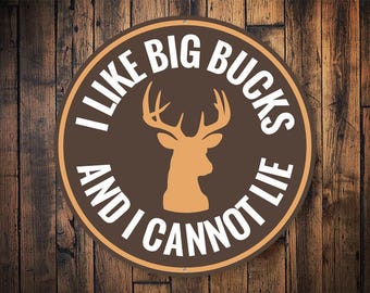 May include: A brown and white round metal sign with the text "I like big bucks and I cannot lie" in white lettering. A brown silhouette of a deer head is in the center of the sign.