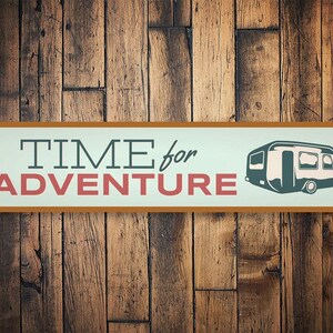 May include: A brown and orange metal sign with the text "TIME for ADVENTURE" in white and red letters. A cartoon image of a camper van is on the right side of the sign.