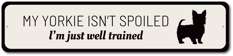 May include: A white sign with black text and a black silhouette of a Yorkshire Terrier. The text reads "My Yorkie isn't spoiled I'm just well trained."