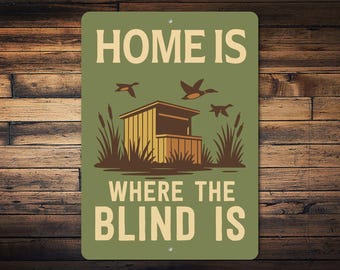 Może przedstawiać: Prostokątny metalowy znak z napisem "HOME IS WHERE THE BLIND IS" w kremowych literach. Znak przedstawia ilustrację czatowni z latającymi kaczkami i trzcinami, na zielonym tle.