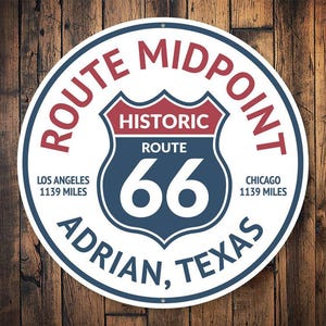 Puede incluir: Un letrero redondo blanco con acentos azules y rojos. El letrero dice "Route Midpoint Historic Route 66 Adrian, Texas" con las distancias "Los Angeles 1139 Miles" y "Chicago 1139 Miles".