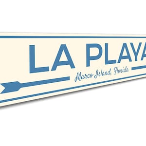 May include: A blue and white metal sign with the text "LA PLAYA" and "Marco Island, Florida". An arrow points to the right.