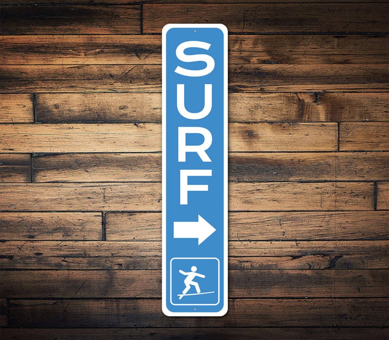Pode incluir: Uma placa azul e branca com a palavra "SURF" escrita verticalmente em letras brancas. Uma seta apontando para a direita est&aacute; abaixo da palavra. Uma silhueta branca de uma pessoa surfando est&aacute; no canto inferior direito da placa.