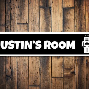 Może przedstawiać: Czarno-biały znak na drzwi z napisem "JUSTIN'S ROOM" i grafiką robota.
