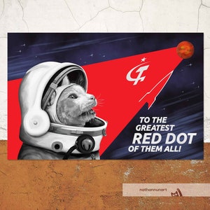 Peut inclure: Affiche avec un chien portant un casque d'astronaute blanc sur un fond rouge et bleu marine. Le texte dit "TO THE GREATEST RED DOT OF THEM ALL !" Une planète rouge est visible en haut à droite.
