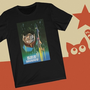 May include: Black t-shirt featuring a graphic of a cat wearing a space helmet and a rocket ship. The text on the graphic reads "We see no borders here to peace and prosperity unification we go!"