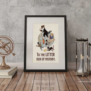 May include: A framed art print with a humorous illustration of cats on a globe, accompanied by the text "TO THE LITTER BOX OF HISTORY." The print is in a black frame, displayed with a brass armillary sphere, books, and hourglasses.