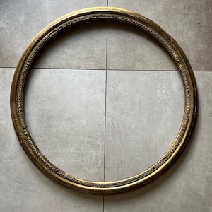 May include: A circular, ornate gold-colored picture frame. The frame has a detailed, textured design around the inner and outer edges. The frame is empty, with no picture or artwork inside.