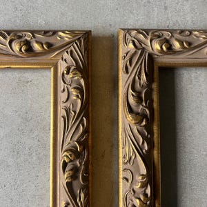Puede incluir: Dos marcos de fotos ornamentados con acabado dorado y beige. Los marcos presentan diseños detallados de flores y hojas talladas. Los marcos están vacíos, listos para obras de arte o fotos.