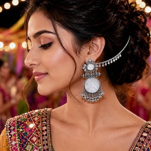May include: A silver-toned earring featuring a circular white stone, intricate metalwork, and a delicate chain that connects to the hair. The earring has a dangling design with small silver beads at the base and a floral-inspired top component.