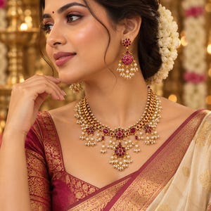 May include: A gold-toned necklace and matching drop earrings set featuring circular motifs inlaid with deep pink stones. The jewelry is accented with small white pearl beads arranged in delicate clusters along the edges of the necklace and earrings.