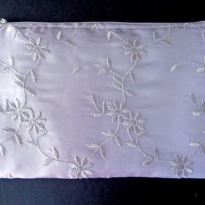 May include: A light purple satin pouch with a floral embroidery design. The pouch has a zipper closure and a tassel. The embroidered flowers and vines are in a lighter shade of purple.