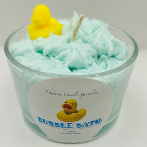 Puede incluir: Una vela de vidrio transparente con un diseño de cera batida azul claro, rematada con un patito de goma amarillo. La vela tiene una etiqueta que dice "Bubble Bath" y "Chateau Candle Specialists". La vela pesa 113g.