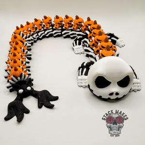 May include: A 3D-printed Halloween decoration featuring a stylized Jack Skellington head and a segmented body of pumpkins and black and white stripes. The pumpkins are orange with brown stems. The decoration is on a white surface.