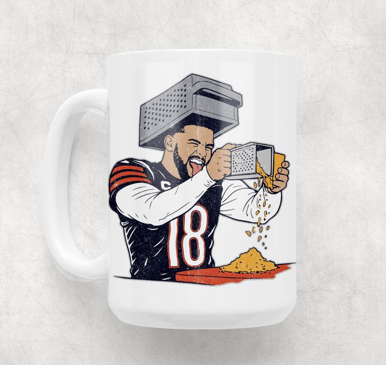 May include: White ceramic mug featuring a cartoon illustration of a football player wearing a grater on his head and grating cheese. The player is wearing a black and orange jersey with the number 18. The mug has a white handle.
