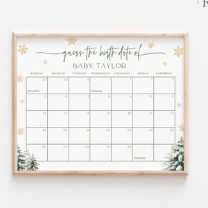 May include: A framed calendar print with the text "guess the birth date of BABY TAYLOR." The calendar grid is green on a white background, with gold snowflake and tree accents. The frame is light brown.