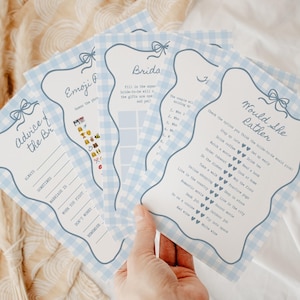 May include: A set of rectangular bridal shower game cards featuring a light blue and white gingham border with a bow illustration at the top. The cards include titles such as Advice for the Bride, Emoji Pictionary, and Would She Rather with text.