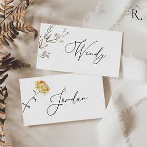 Peut inclure: Deux cartes de place blanches avec des illustrations florales et des noms &eacute;crits &agrave; la main. La carte du haut a une petite branche de fleurs roses et le nom "Wendy". La carte du bas a une fleur jaune et le nom "Jordan".