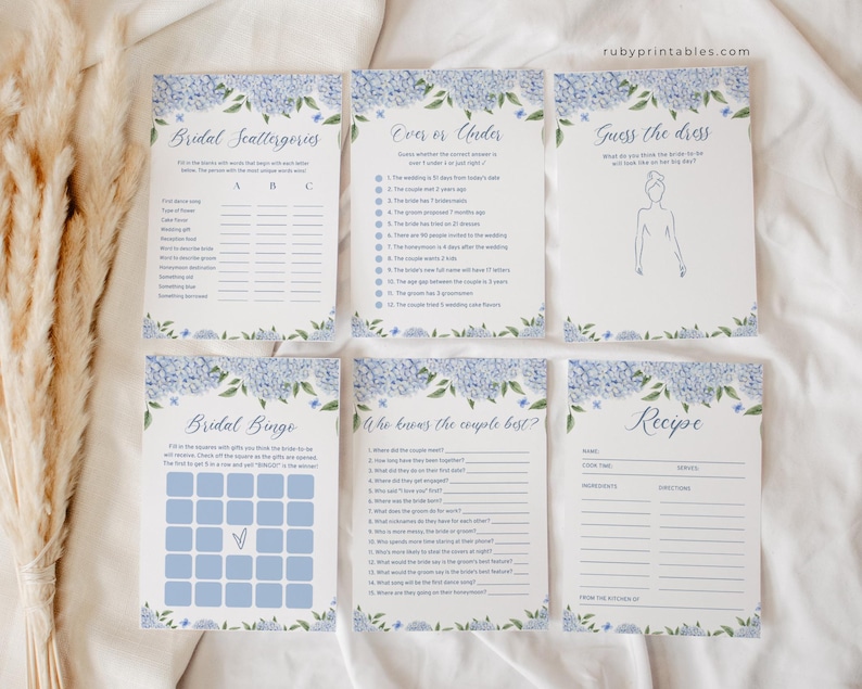 Puede incluir: Seis tarjetas de juegos para una despedida de soltera con un dise&ntilde;o floral azul. Los juegos incluyen "Bridal Scattergories", "Over or Under" y "Guess the Dress". El sitio web "rubyprintables.com" es visible. Para una boda.
