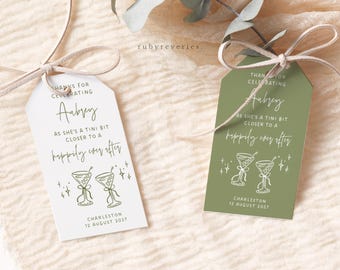 Può includere: Due etichette regalo a tema cocktail. Un'etichetta è bianca, l'altra verde oliva. Entrambe le etichette riportano il testo "Grazie per aver festeggiato Aubrey" e "Mentre si avvicina un po' di più a un lieto fine". Le etichette includono anche la data e il luogo.
