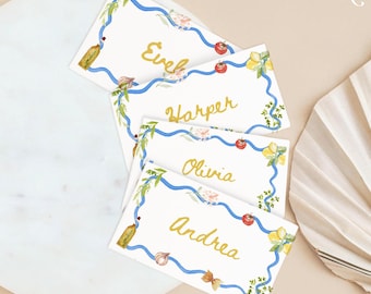 Puede incluir: Cuatro tarjetas de lugar con cinta azul y diseños florales. Los nombres "Eve", "Harper", "Olivia" y "Andrea" están escritos en letras doradas.