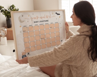 May include: A framed calendar with the text "guess the mood date of BABY JOSEPHINE" in a decorative font. The calendar grid is peach-colored with days of the week across the top. Decorative elements include a moon, stars, and a bat.