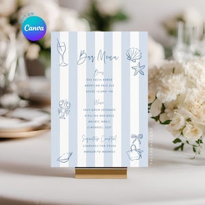 May include: A bar menu card with blue and white stripes, featuring illustrations of seaside elements. The menu lists beer, wine, and cocktails. The card is held in a gold-colored stand.
