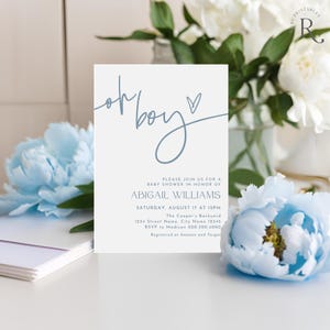 May include: A baby shower invitation with the words "oh boy" in a script font, with a heart symbol. The invitation includes details for Abigail Williams' baby shower, including the date, time, and location. The invitation is light blue.