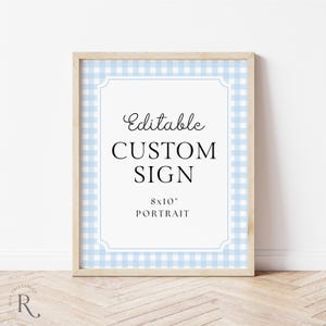 Puede incluir: Un letrero enmarcado con un marco de madera clara. El letrero tiene un centro blanco con las palabras "Editable CUSTOM SIGN" en escritura negra y letras en bloque. El fondo es un patrón de cuadros vichy azul claro. El letrero mide 20,3 x 25,4 cm.