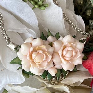 May include: A silver chain necklace with a pendant featuring two pink flower blossoms with green leaves.